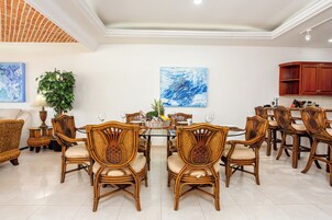 Uma área de refeições com cadeiras de vime, uma mesa de vidro e um vaso de planta.