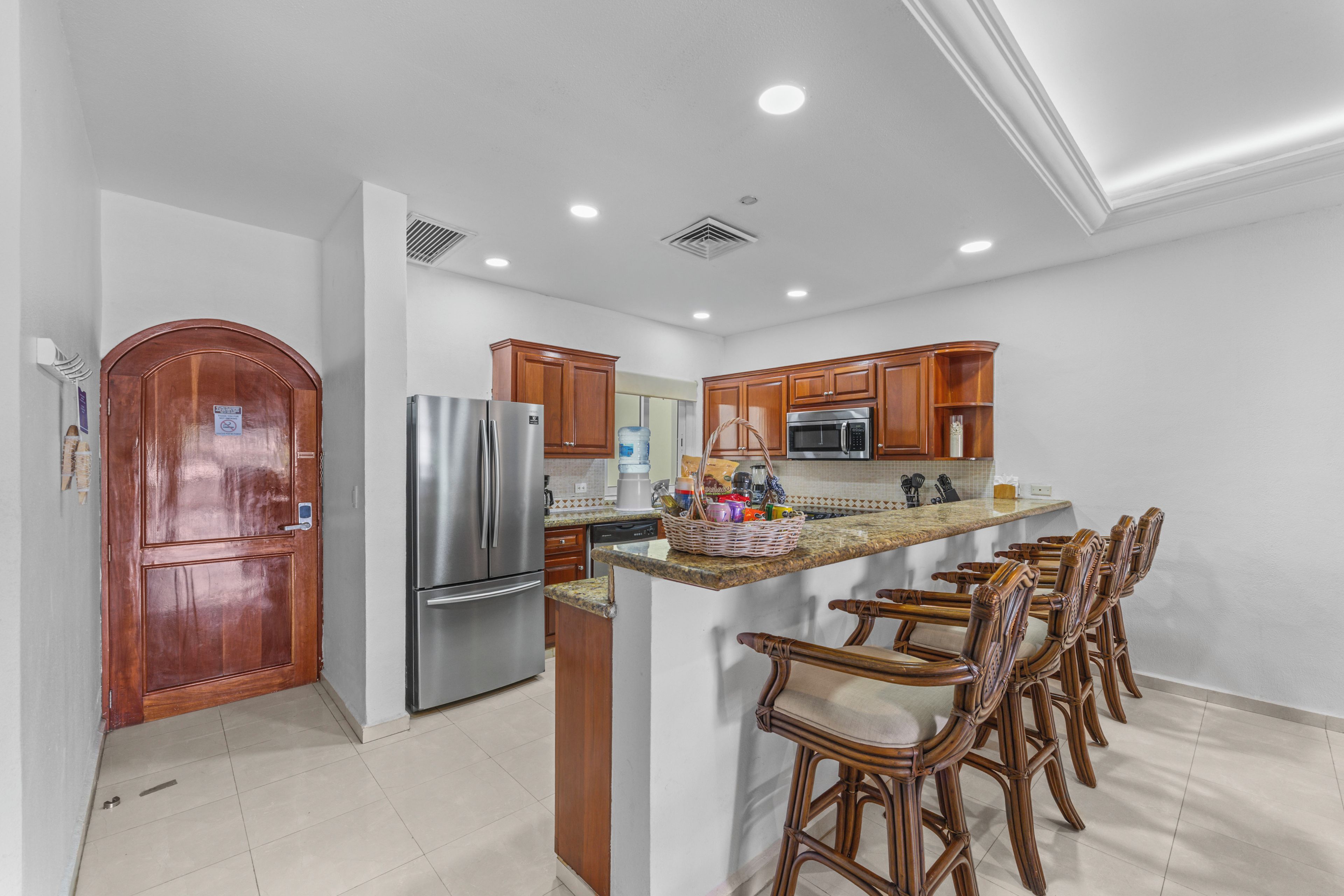 Una cocina con refrigerador de acero inoxidable, armarios de madera, microondas y barra desayunadora con taburetes.