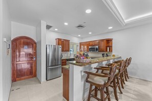 A kitchen with a stainless steel refrigerator, wooden cabinets, a microwave, and a breakfast bar with bar stools. - Aventuras Club Lagoon (Puerto Aventuras)