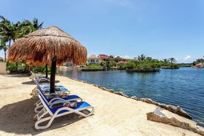 A beachside resort with lounge chairs, a thatched umbrella, and a calm water body. - Aventuras Club Lagoon (Puerto Aventuras)