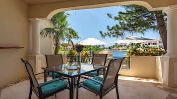 Una mesa con cubierta de vidrio, cuatro sillas, vista a una piscina y palmeras.