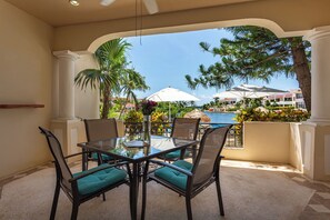 Una mesa con cubierta de vidrio, cuatro sillas, vista a una piscina y palmeras.