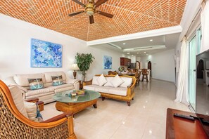 A spacious living area with a ceiling fan, two sofas, a coffee table, and a dining area with chairs. - Aventuras Club Lagoon (Puerto Aventuras)