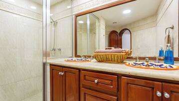 A bathroom with a large mirror, wooden cabinets, a sink with decorative tiles, and a shower area.