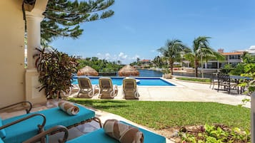 Zona de piscina con sillones de descanso y una sombrilla de paja.
