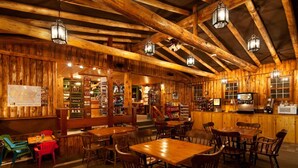 A rustic wooden interior with exposed beams, wooden tables and chairs, and hanging lanterns. - Snake River Cabin Village (Jackson)