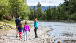 A family walking along a rocky riverbank with a forest in the background. - Snake River Cabin Village (Jackson)