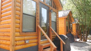 A log cabin with a wooden exterior, large windows, and a set of wooden stairs leading to the entrance. - Snake River Cabin Village (Jackson)