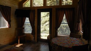A cozy cabin room with a wooden interior, a dining table with a fruit-patterned tablecloth, and a large window with curtains. - Snake River Cabin Village (Jackson)