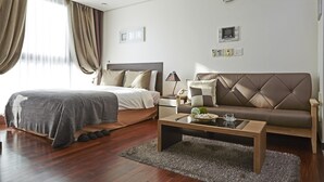 A modern hotel room with a bed, a sofa, a coffee table, and a large window with curtains. - Brown Suites Seoul (Seoul)