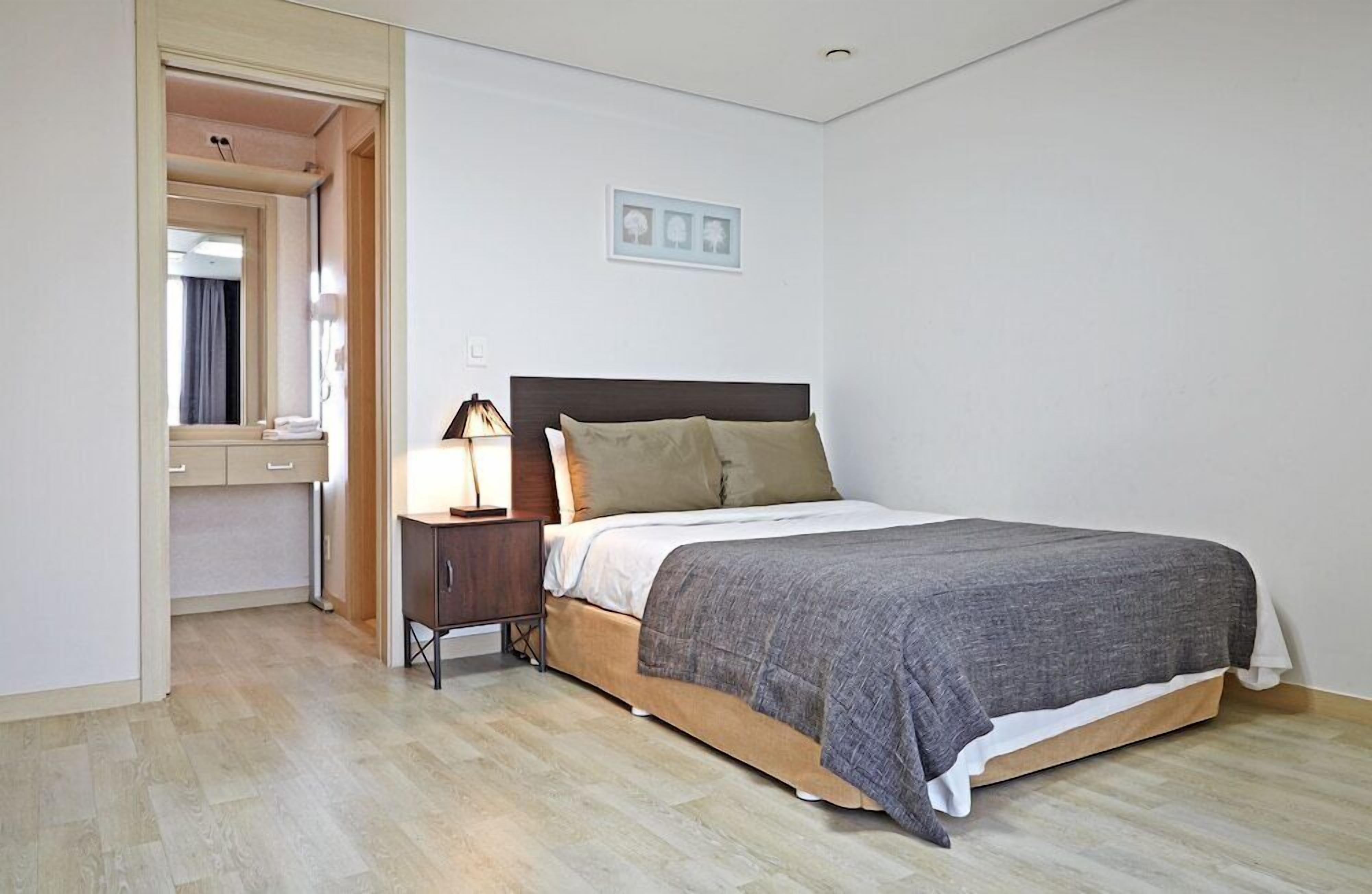 Een slaapkamer met een bed, nachtkastje en spiegel.