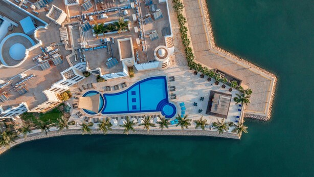 An aerial view of a resort with a large pool, sun loungers, and palm trees.
