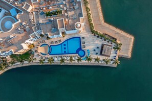 Vista aérea de un resort con una piscina grande, tumbonas y palmeras.