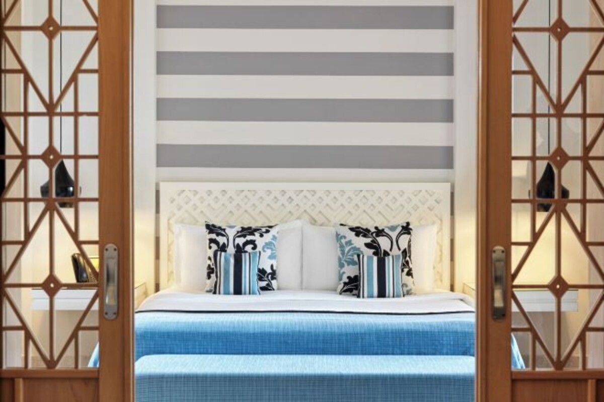 Habitación de hotel con cama, pared a rayas y paneles decorativos.