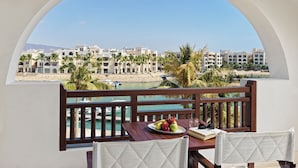 A balcony with a view of a coastal town, a table with fruit and a book, and a chair.
