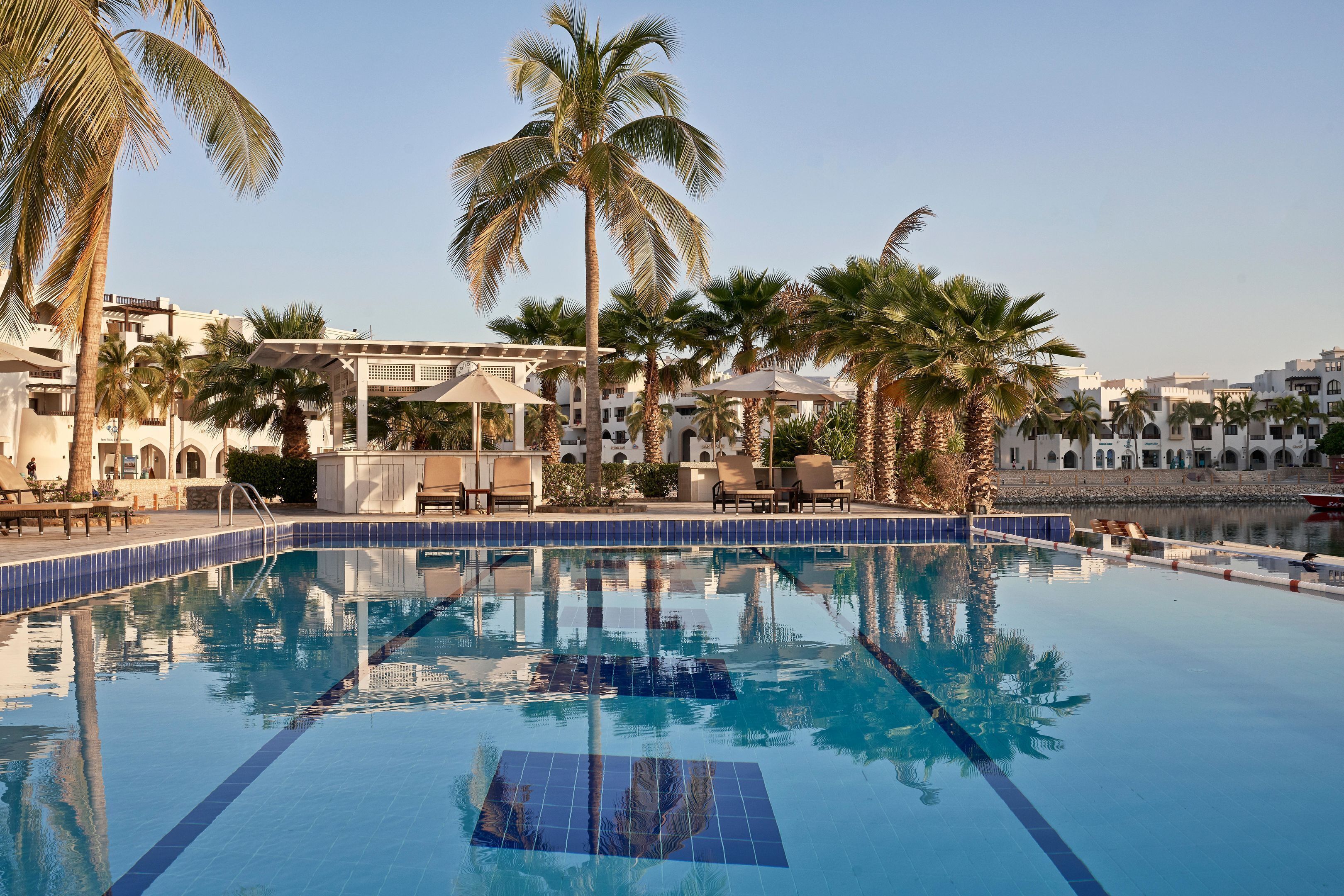 Une piscine à l’eau d’un bleu cristallin, entourée de palmiers et dotée d’un espace détente abrité.