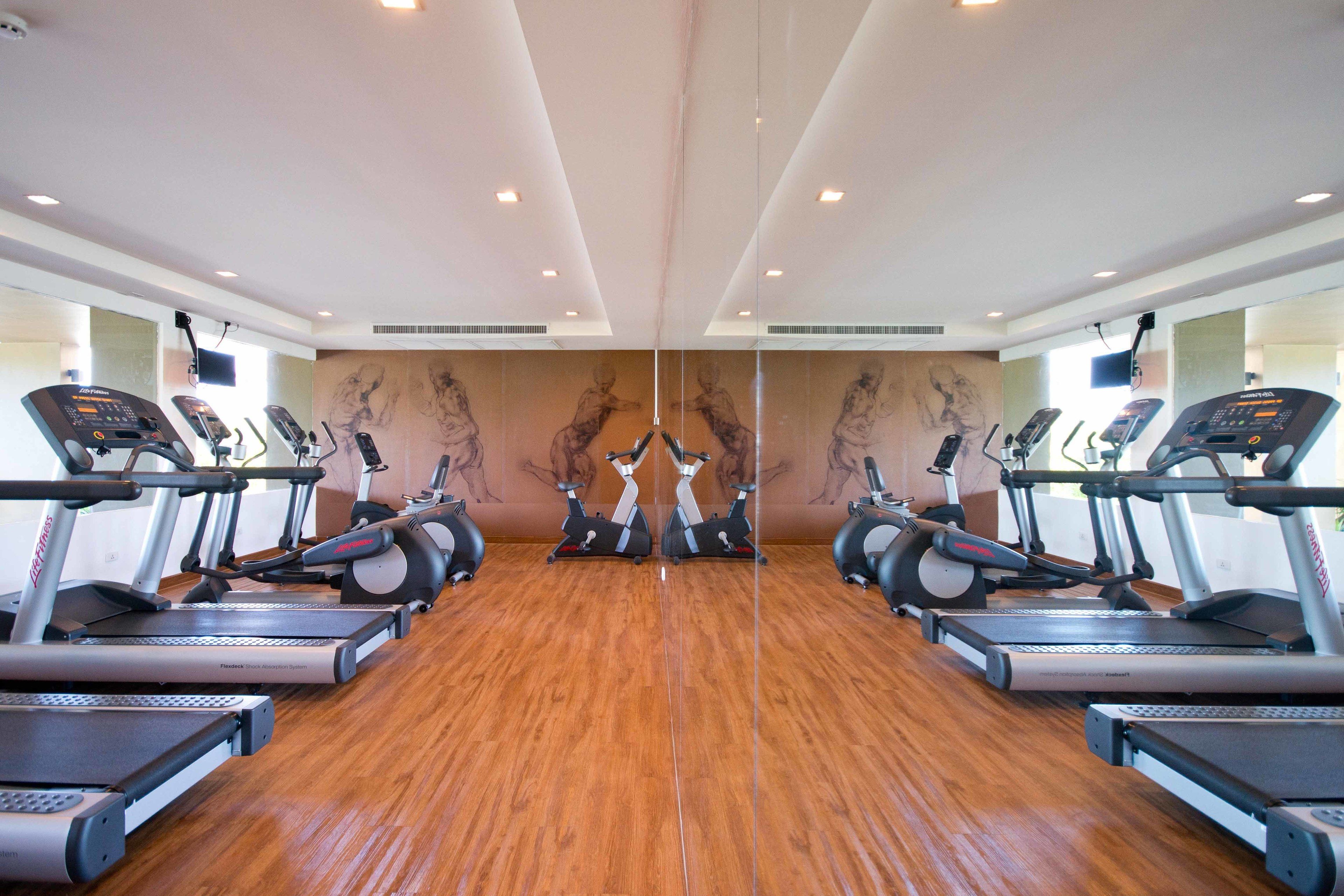 A gym with mirrored walls, exercise equipment, and a wooden floor.