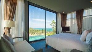 A hotel room with a large bed, a TV, a seating area with a lamp, and a balcony with a view of the ocean. - SUNSURI PHUKET, Nai Harn Beach (Rawai)