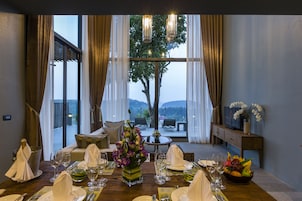 A dining room with a table set for a meal, a vase of flowers, and a view of the outdoors.