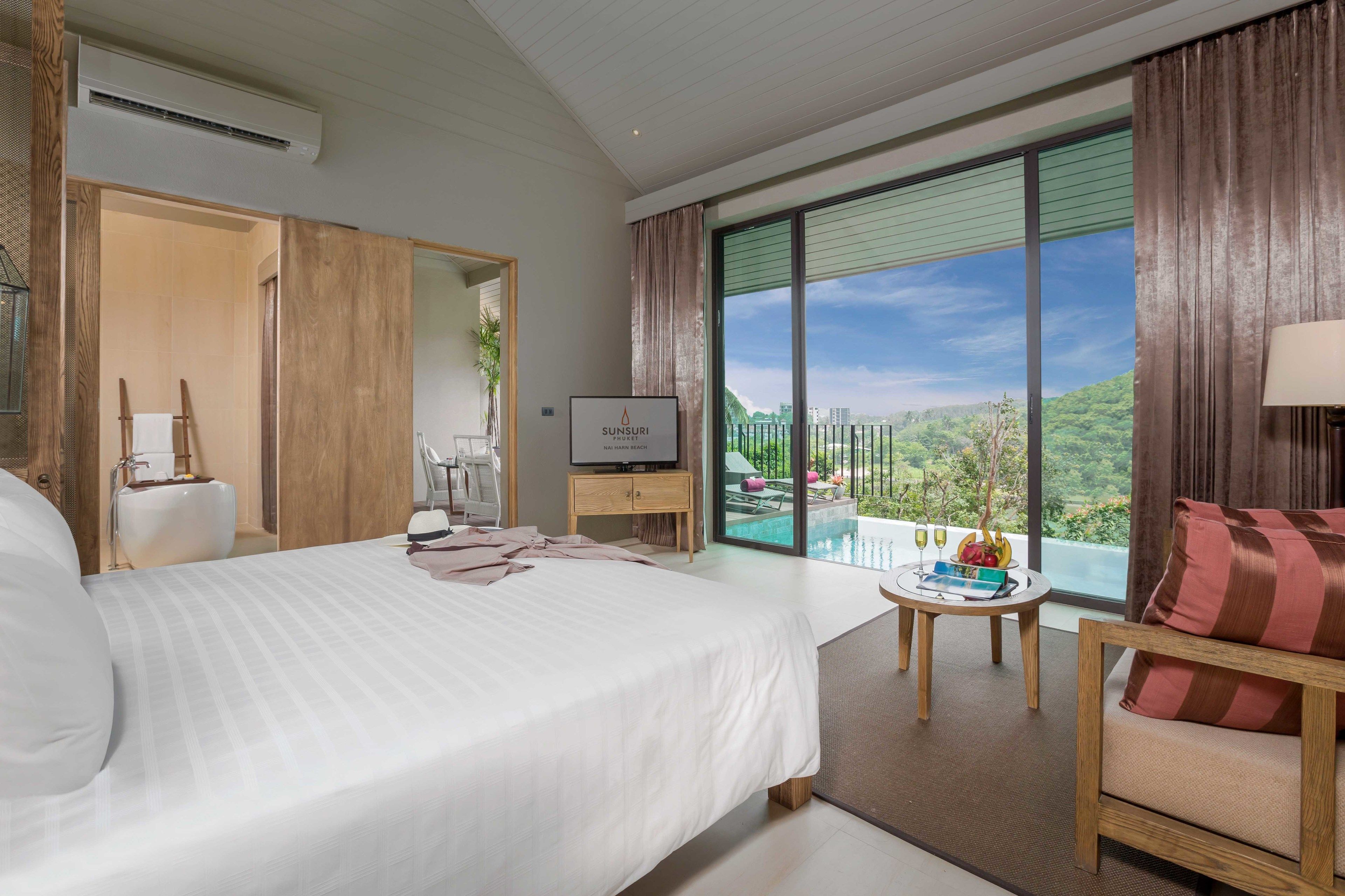 Une chambre d’hôtel moderne avec un grand lit, une télévision, une petite table avec une boisson et un balcon offrant une vue agréable.