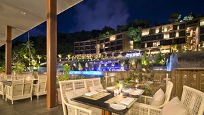 An outdoor dining area with wicker furniture and a pool in the background. - SUNSURI PHUKET, Nai Harn Beach (Rawai)