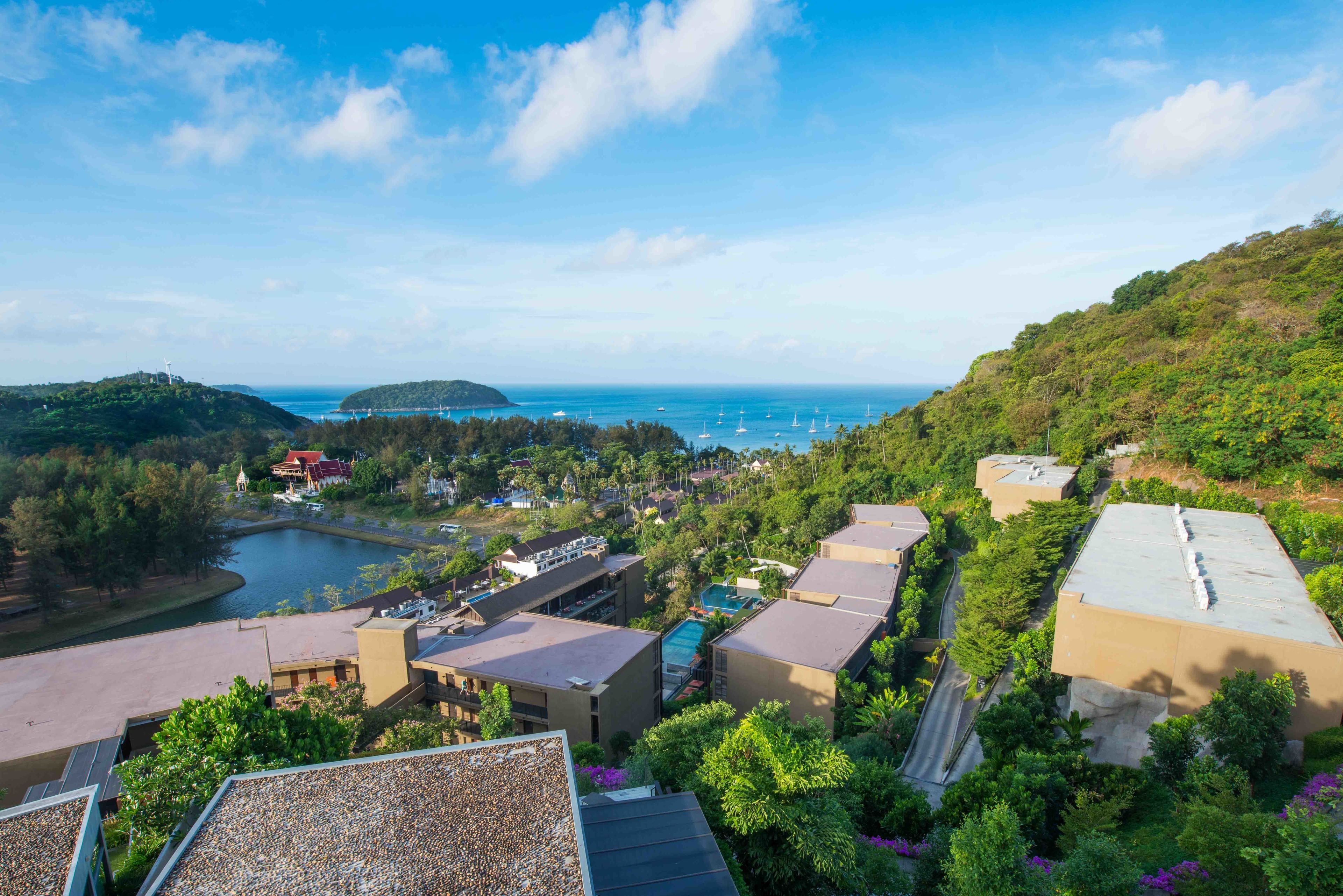 A resort with multiple buildings, a swimming pool, and a view of the sea and hills.