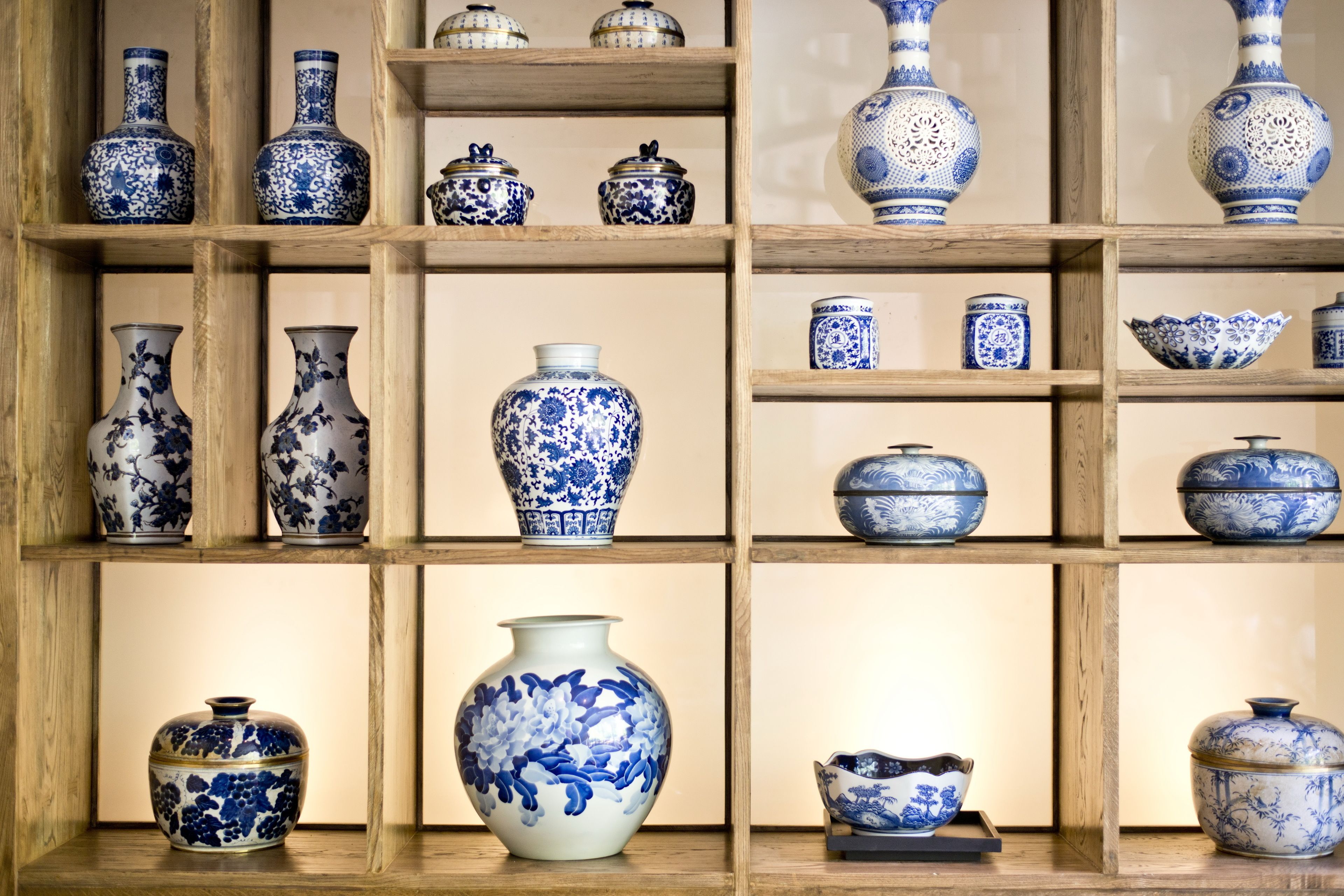 Een presentatie van blauwe en witte keramieken vazen en kommen op houten planken.