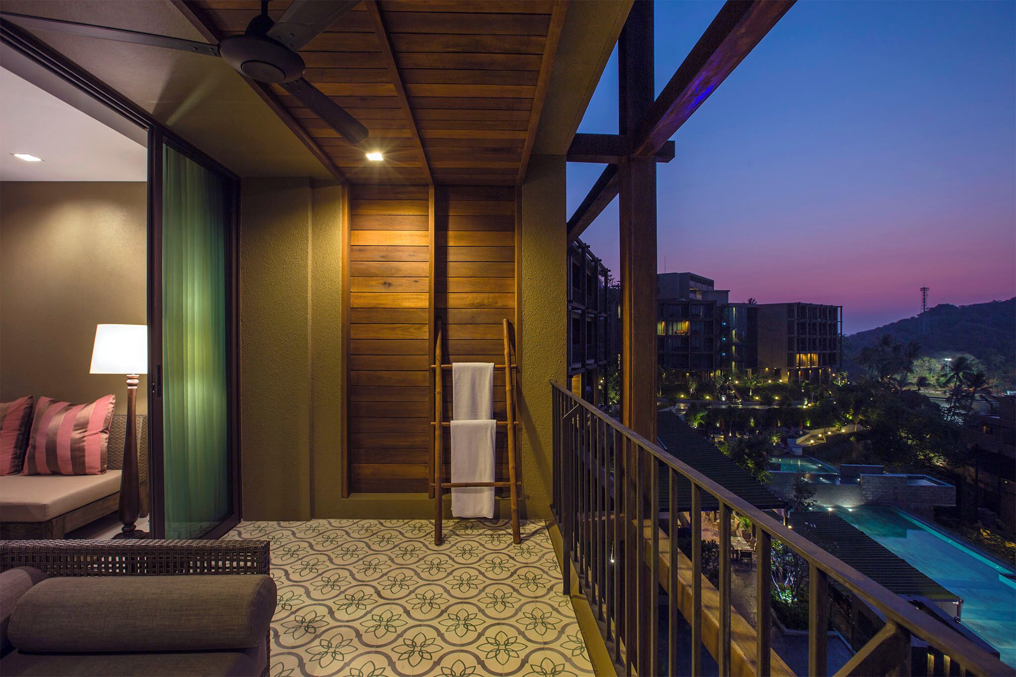 Un balcón con vista a una piscina y edificios al atardecer.
