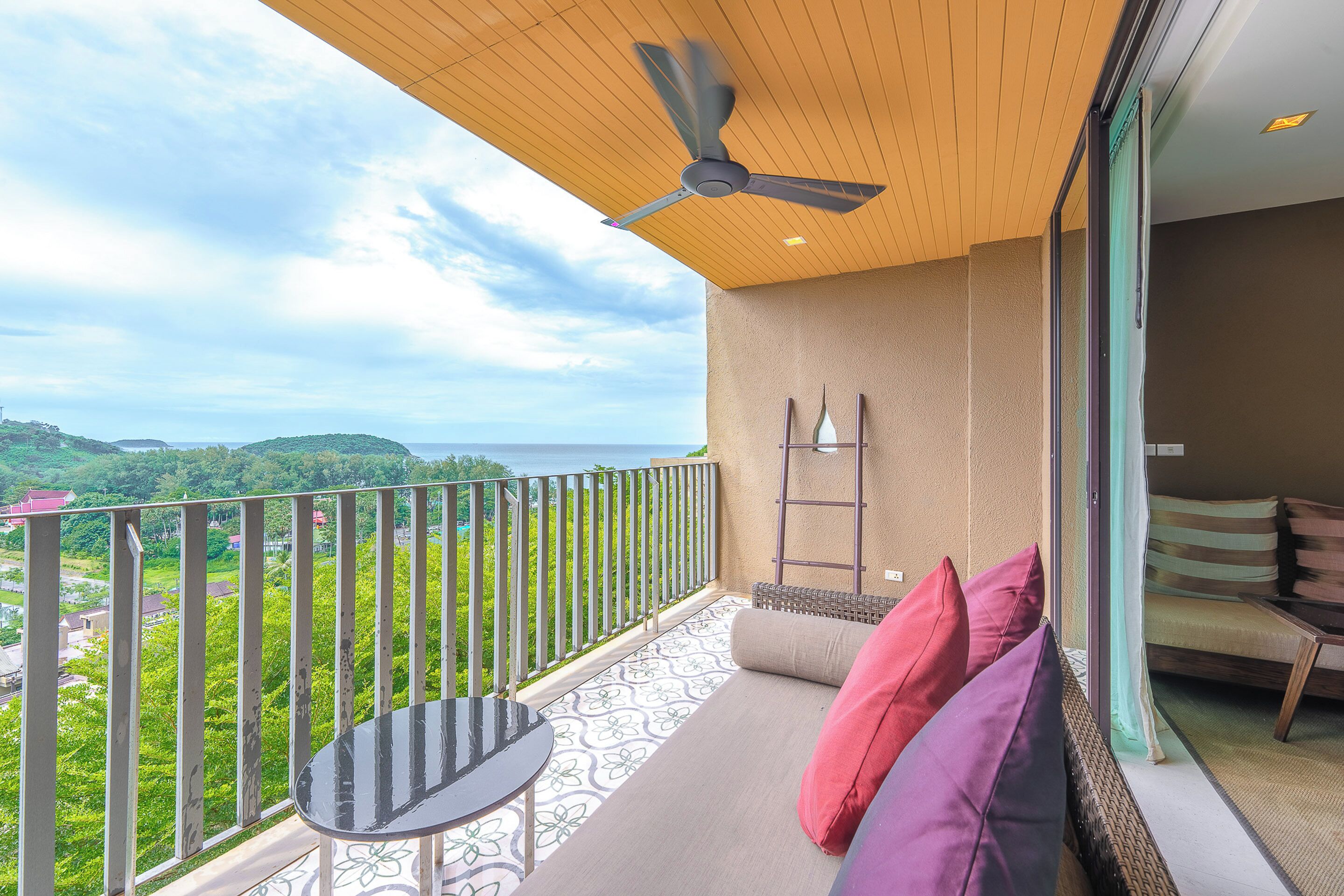 A balcony with a table and chairs, a ceiling fan, and a view of a green landscape.