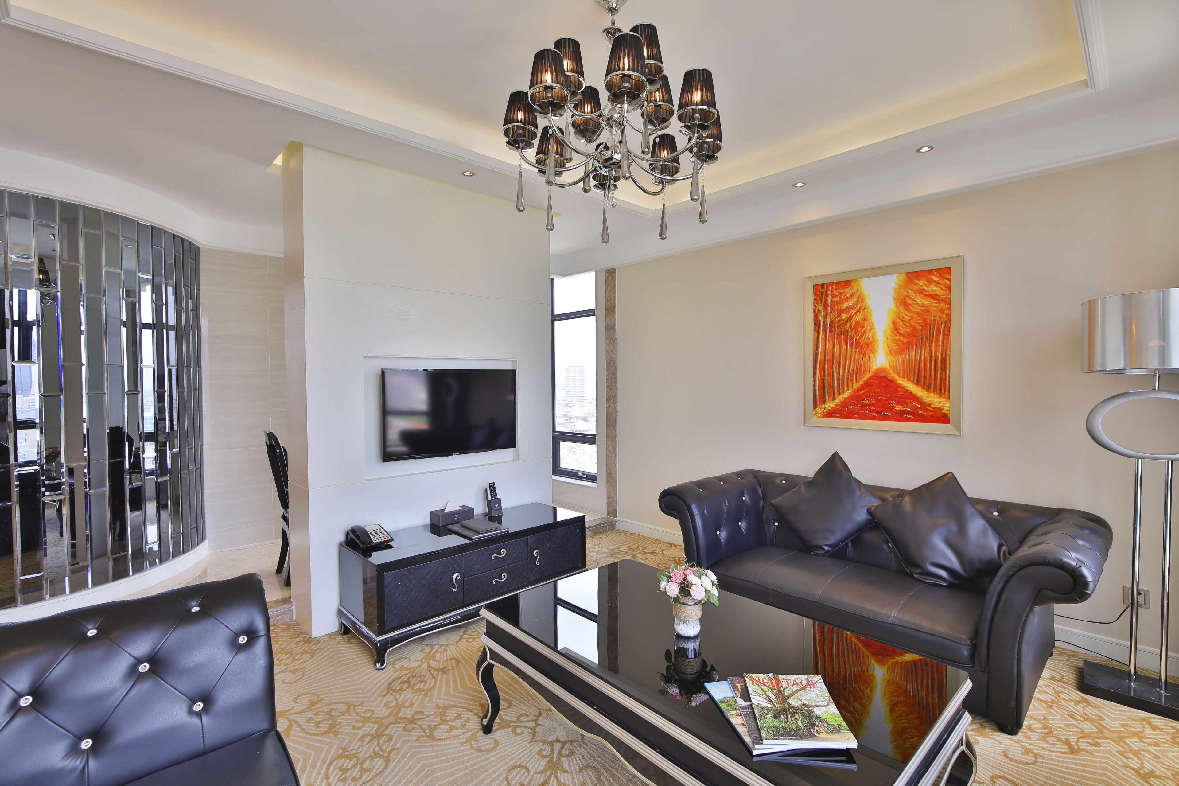 Un salon moderne avec un canapé en cuir noir, une table basse en verre, une console noire, un téléviseur à écran plat et un grand tableau abstrait accroché au mur.