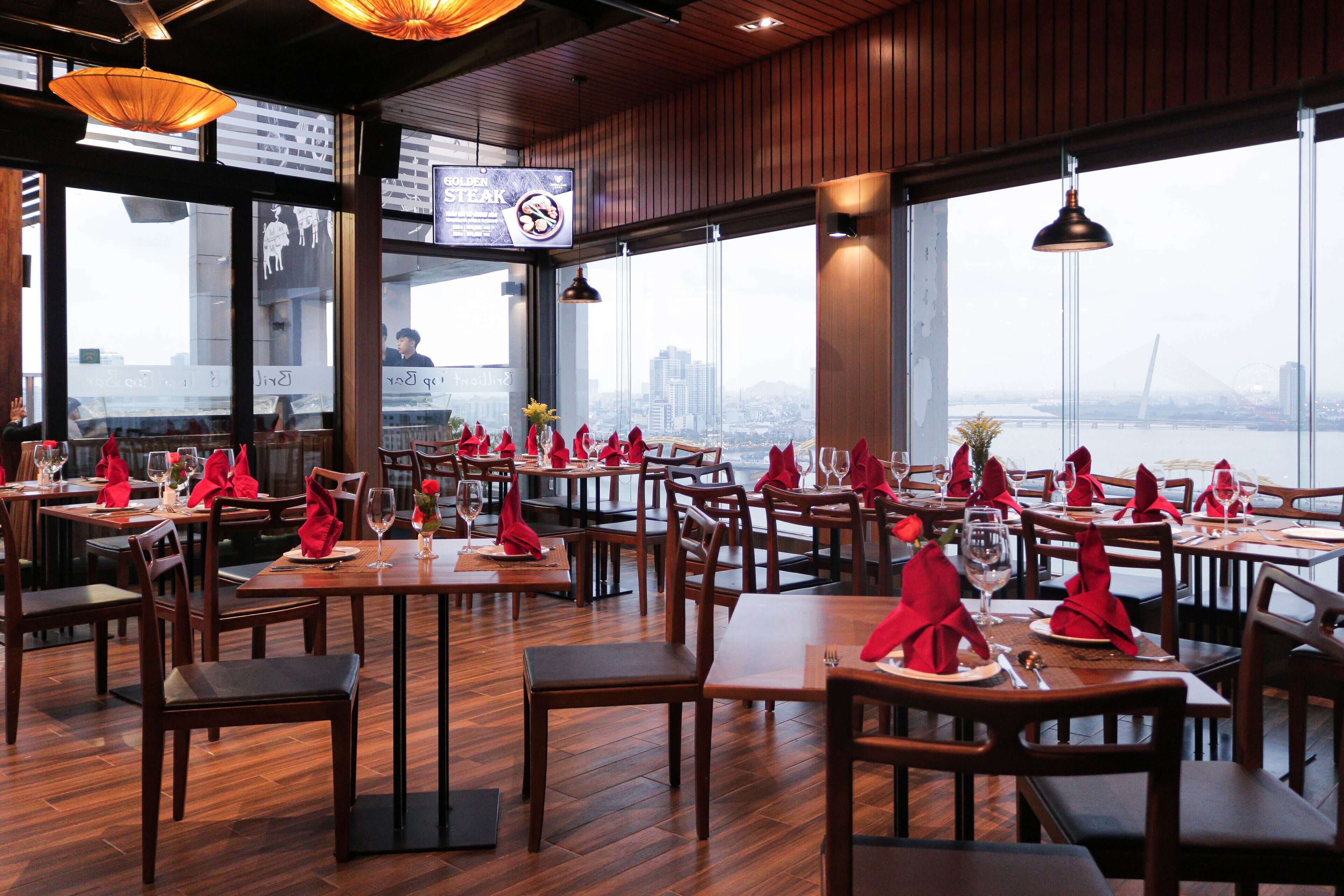 A restaurant with wooden tables and chairs, red napkins, and a view of a cityscape through large windows.