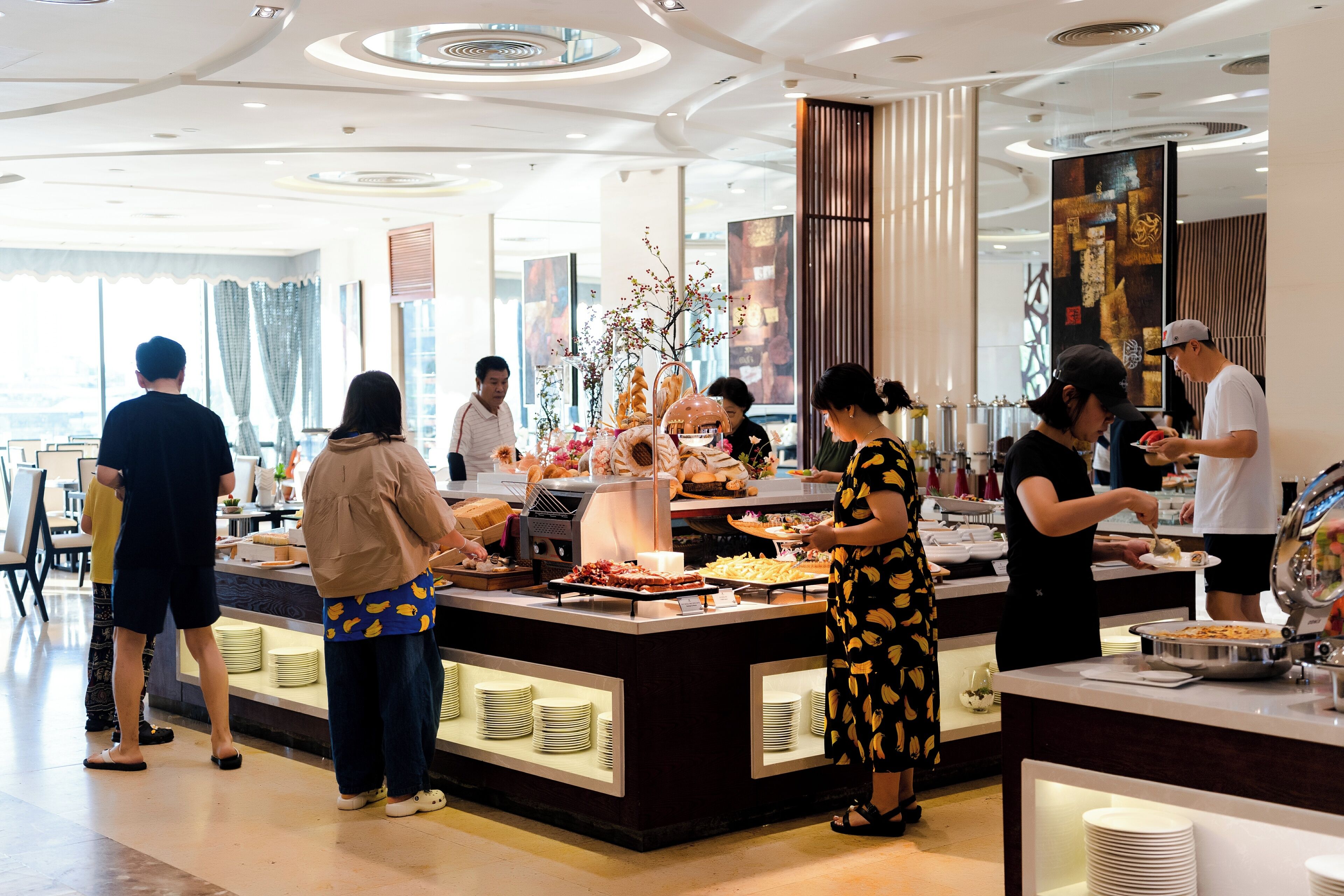 A buffet setup with multiple food stations, a central decorative plant, and a modern interior design.