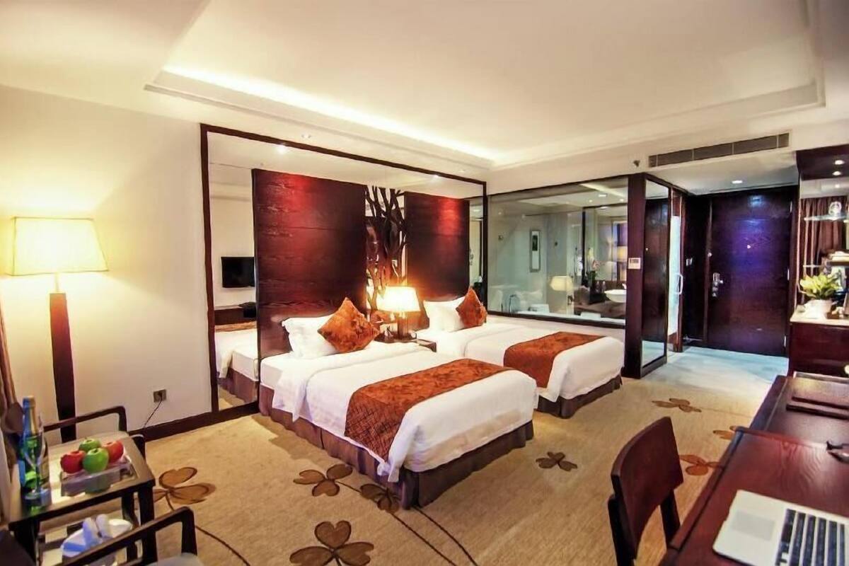 A hotel room with two beds, a desk, a chair, a lamp, and a mirror.