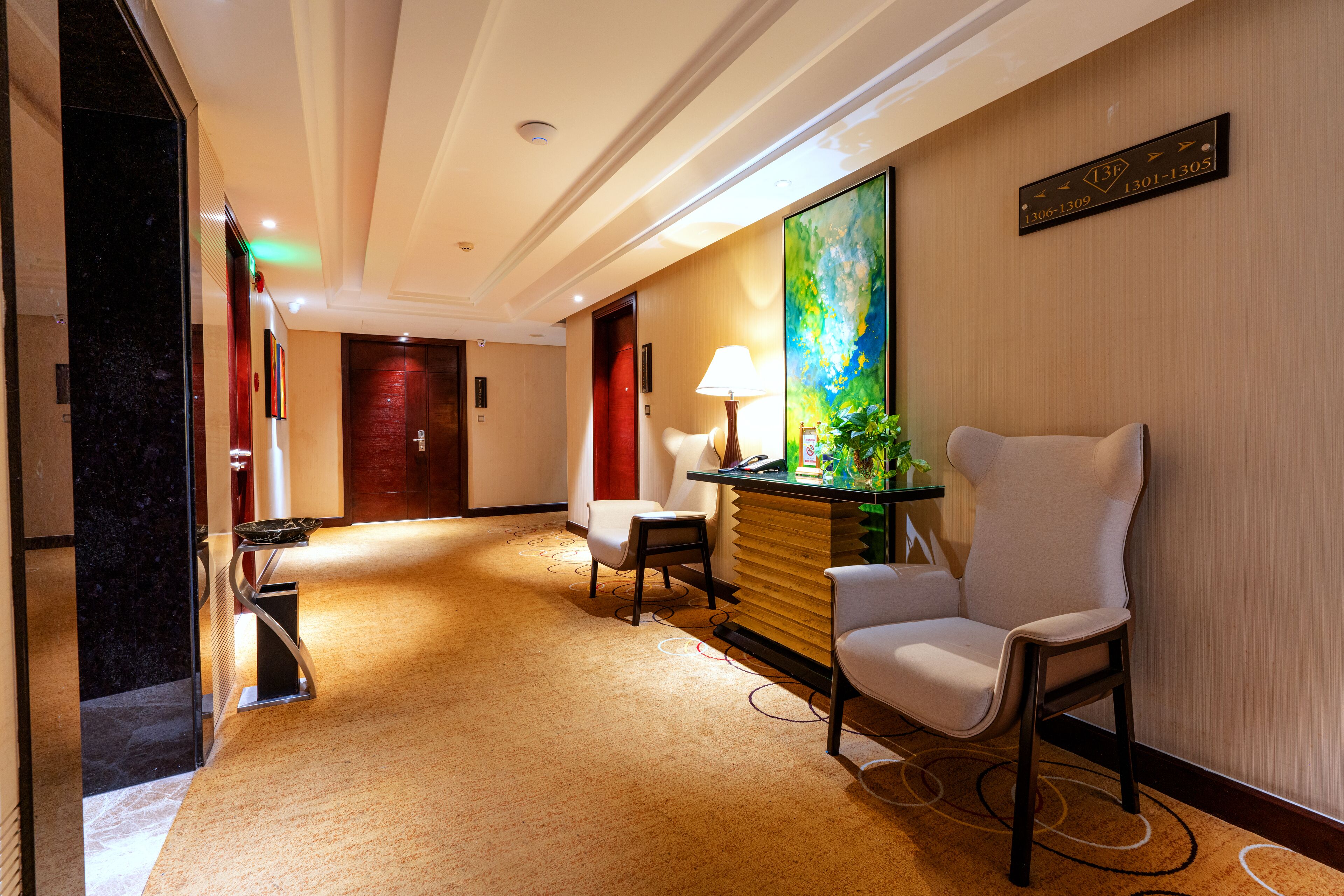 Un hall de hotel con un mostrador de recepción, dos sillones, un cuadro grande y piso alfombrado.