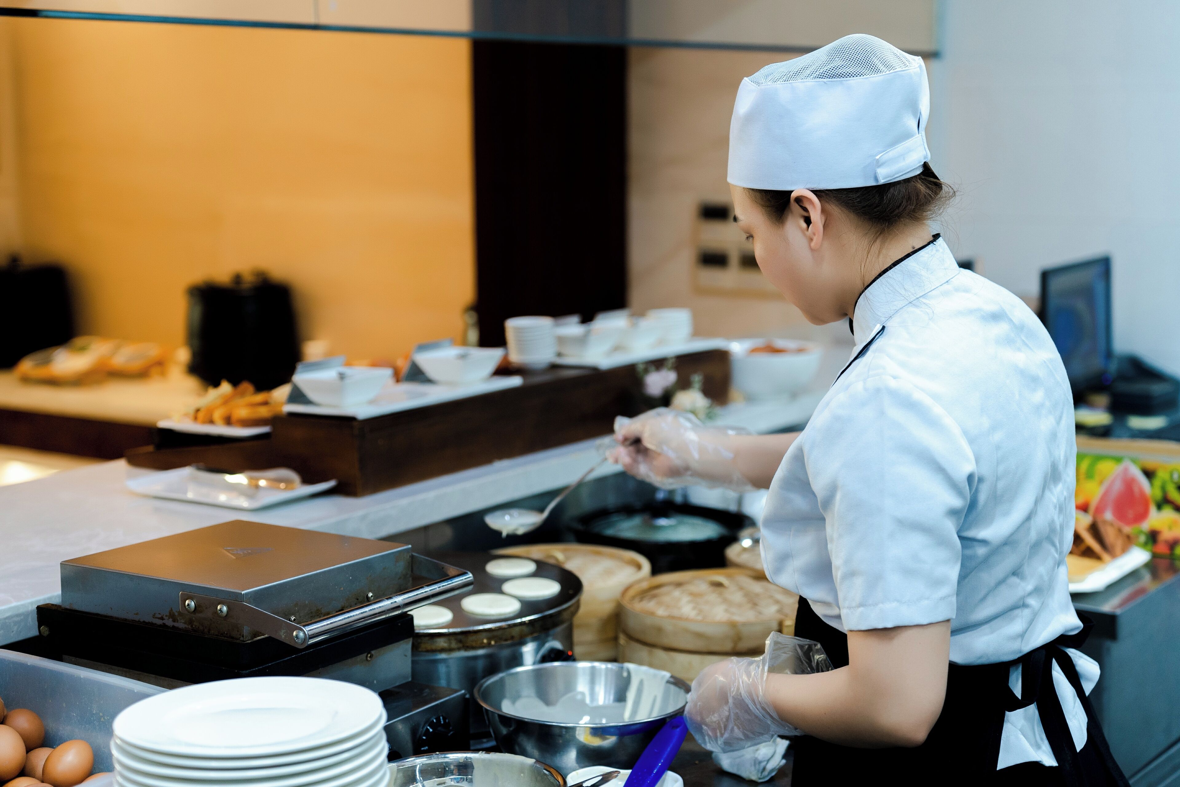 A kitchen area with a cook preparing food, various cooking utensils, and ingredients on the counter.