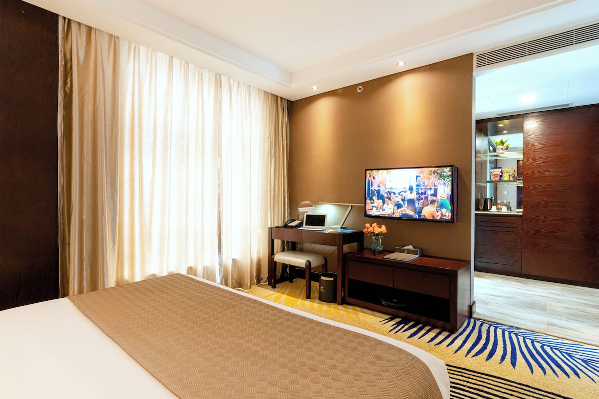 A hotel room with a bed, desk, chair, television, and a small kitchenette.