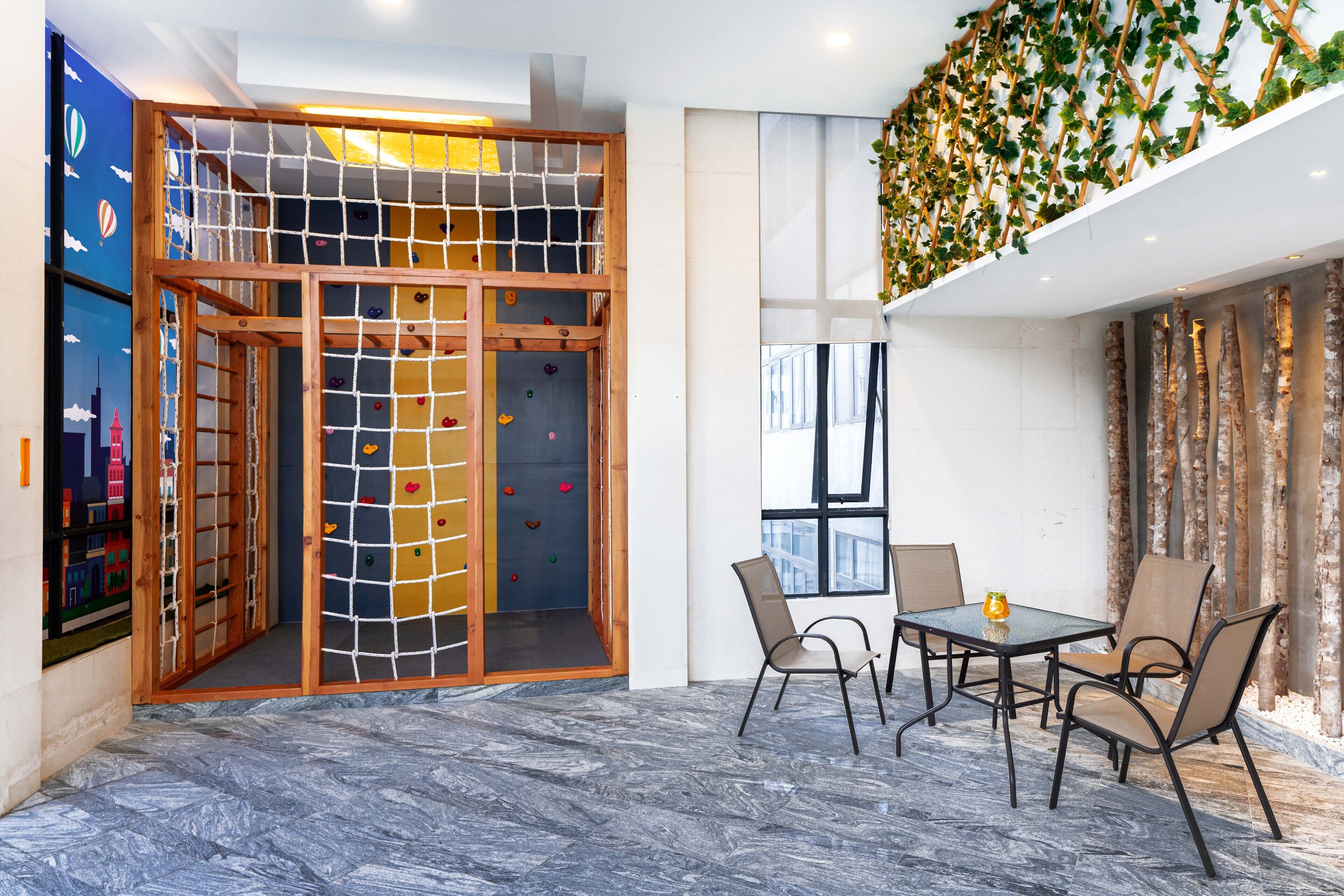 A modern interior with a climbing wall, a dining area with chairs and a table, and a view of the cityscape through large windows.