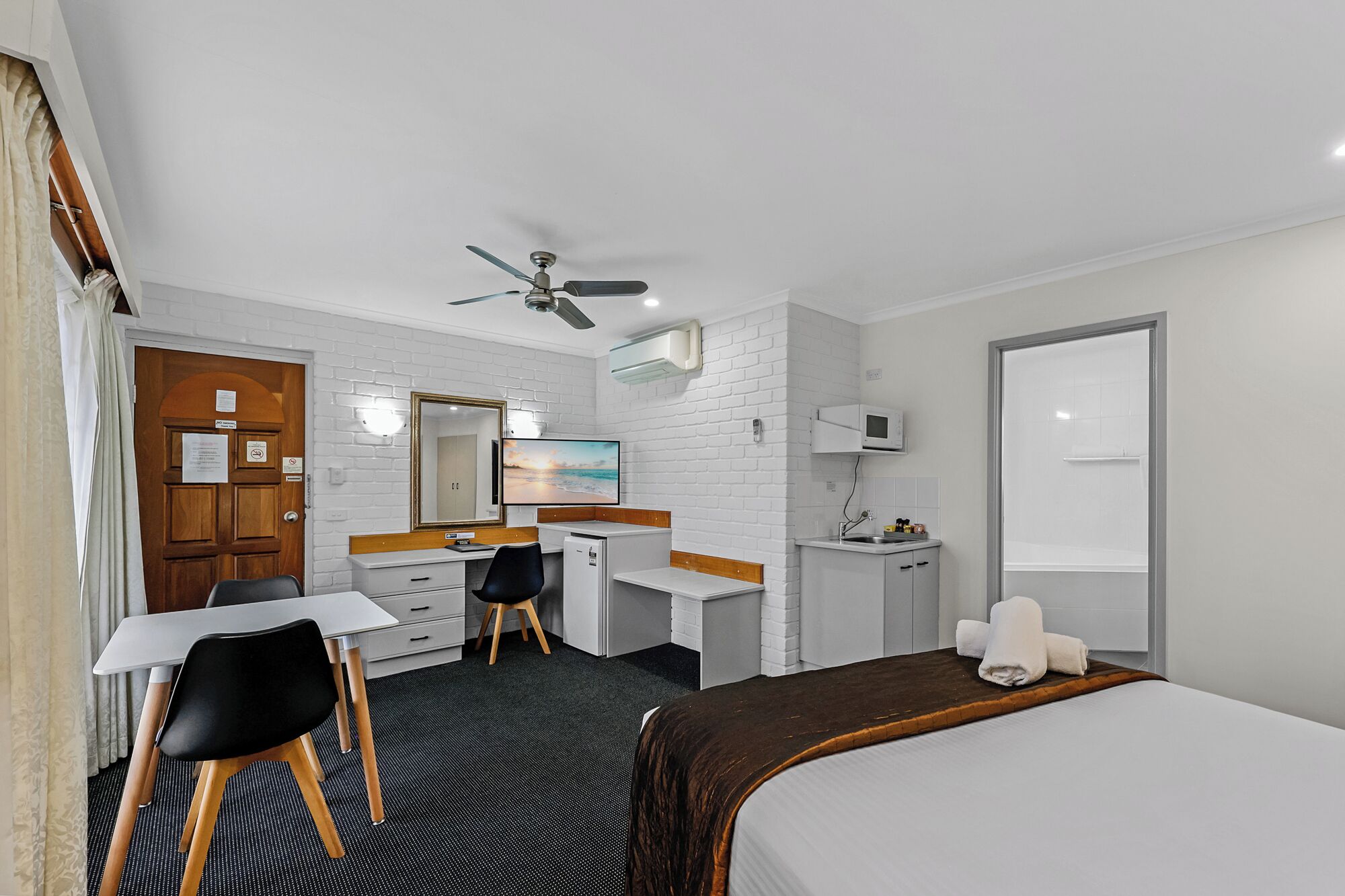 A hotel room with a bed, desk, chair, and a small kitchenette.