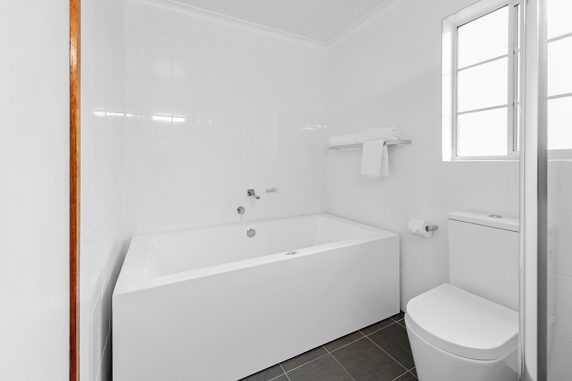 A bathroom with a white bathtub, a toilet, and a window.