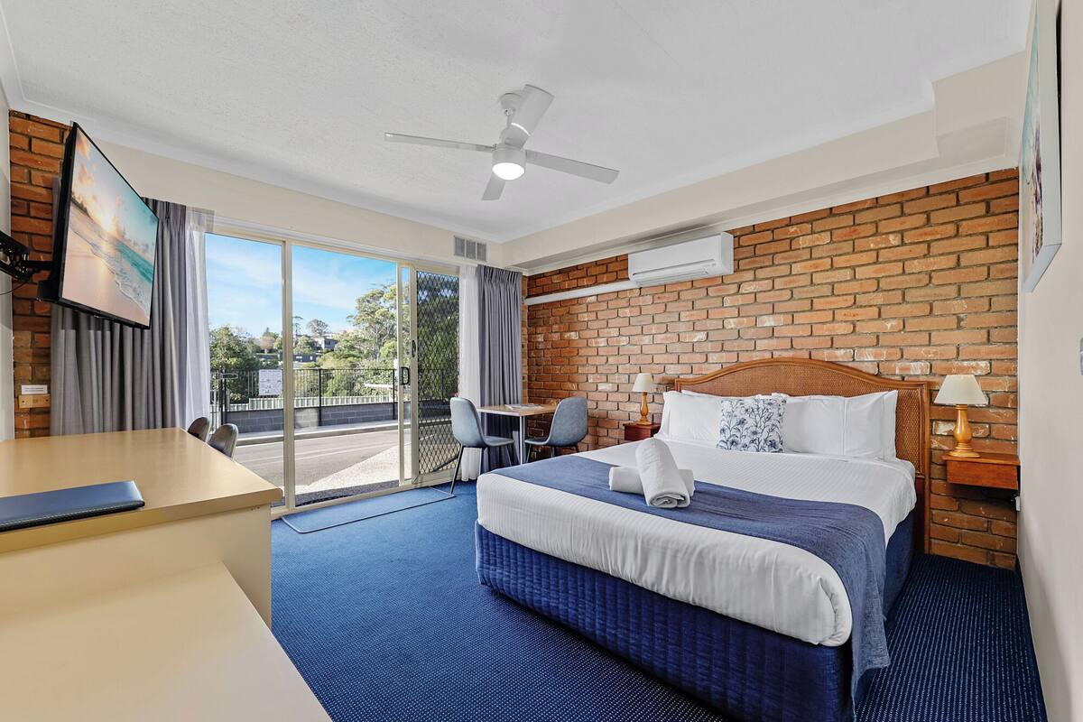 A hotel room with a bed, desk, chair, and a view of the outdoors.