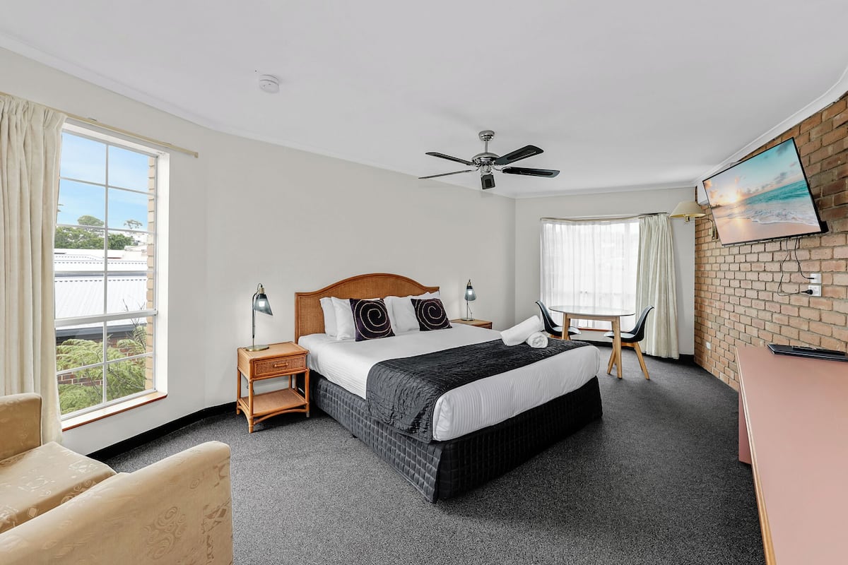 A hotel room with a bed, a desk, a chair, a ceiling fan, and a window with curtains.