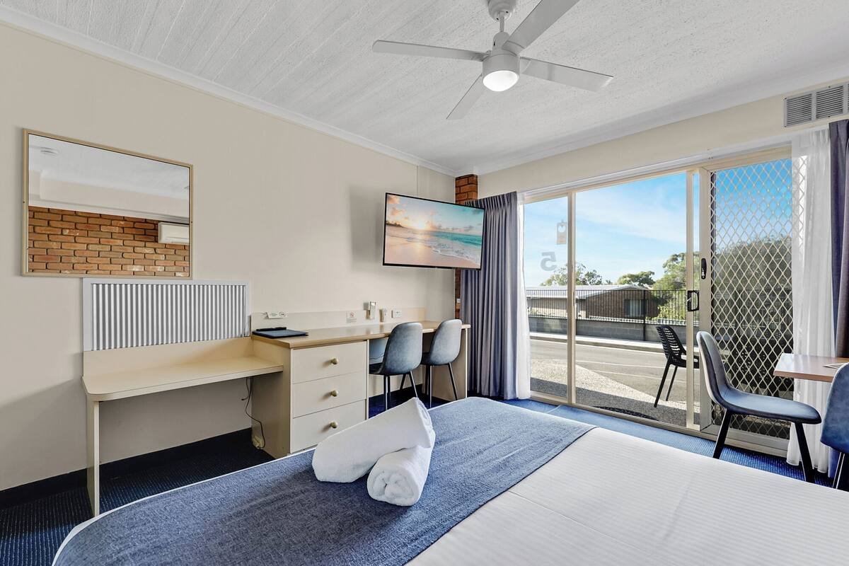 A hotel room with a bed, a desk, two chairs, a television, and a large window with a view of the outside.
