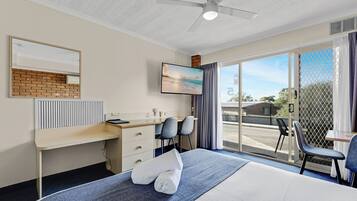 Habitación de hotel con cama, escritorio, dos sillas, televisor y ventana grande con vista al exterior.