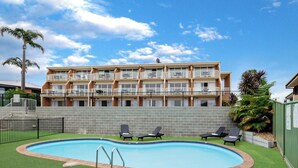 A multi-story building with balconies, a swimming pool, and outdoor seating.
