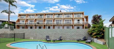 A multi-story building with balconies, a swimming pool, and outdoor seating.