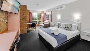 A hotel room with a bed, a desk, a chair, a small table, and a window with curtains.