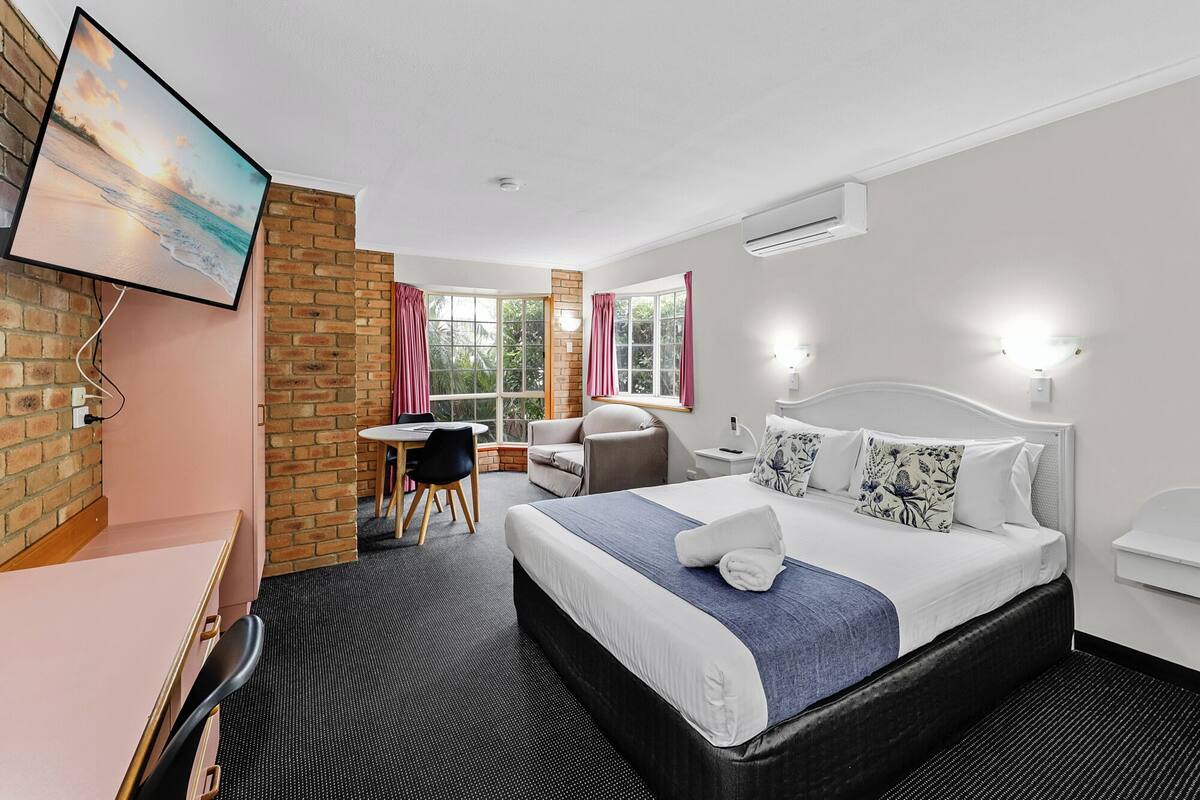 A hotel room with a bed, a desk, a chair, a small table, and a window with curtains.