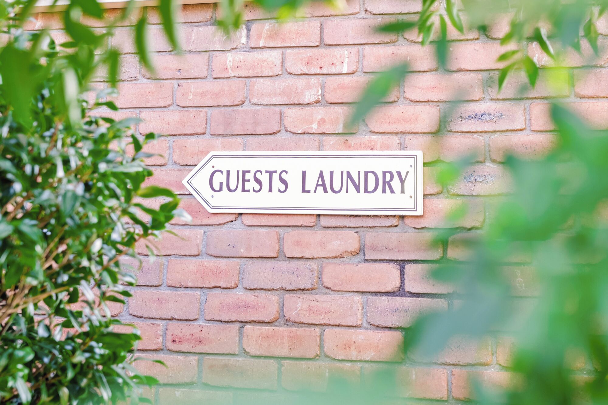 Ein Schild an einer Backsteinmauer mit der Aufschrift 'GUESTS LAUNDRY'.