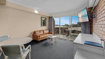 A modern room with a leather sofa, a dining table with chairs, a TV mounted on the wall, and a balcony with a view.