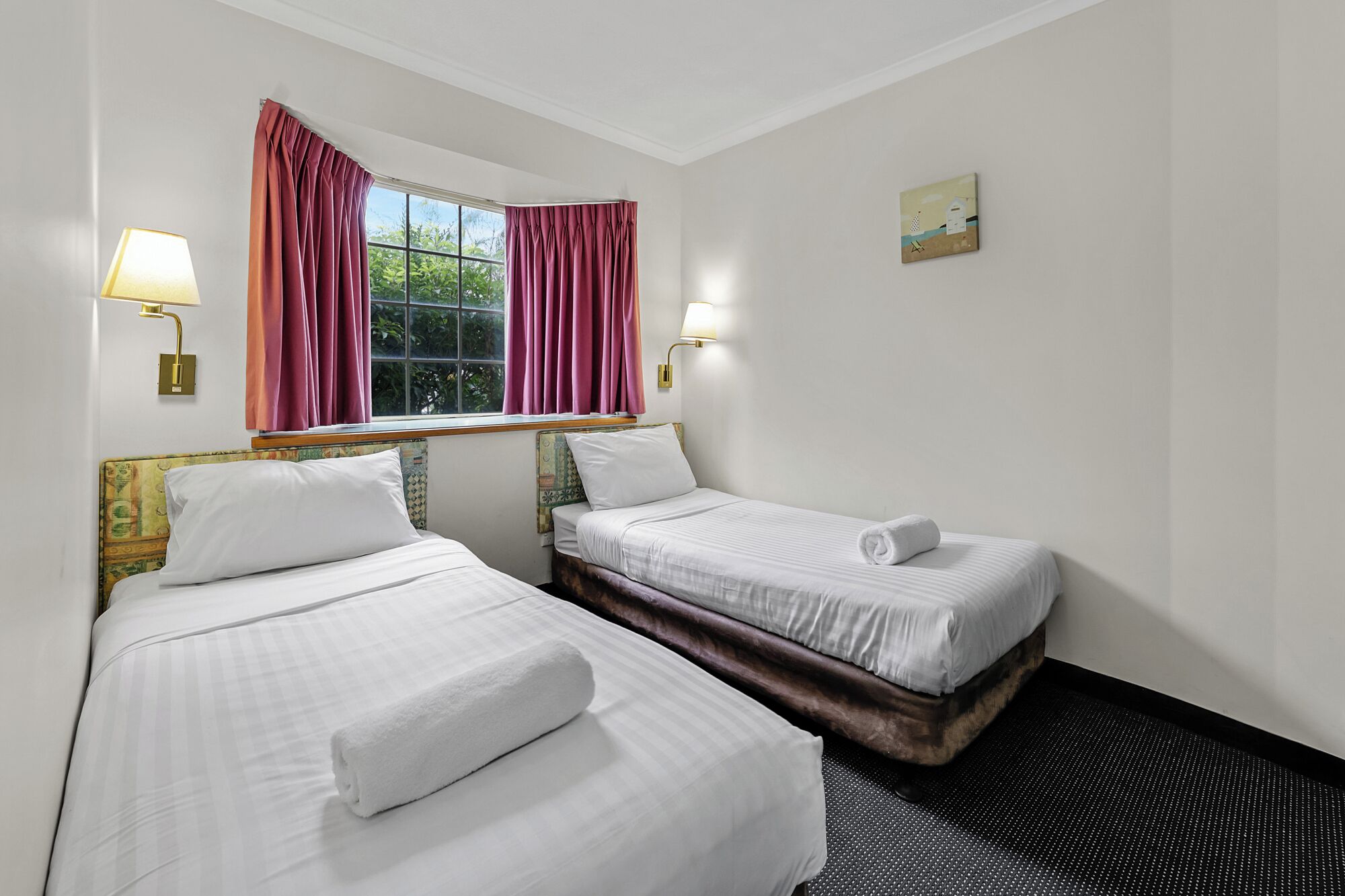 Una habitación de hotel con dos camas, una ventana con cortinas y dos lámparas fijadas a la pared.
